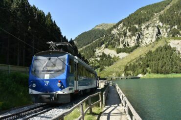 blue and white train on rail tracks near body of water during daytime